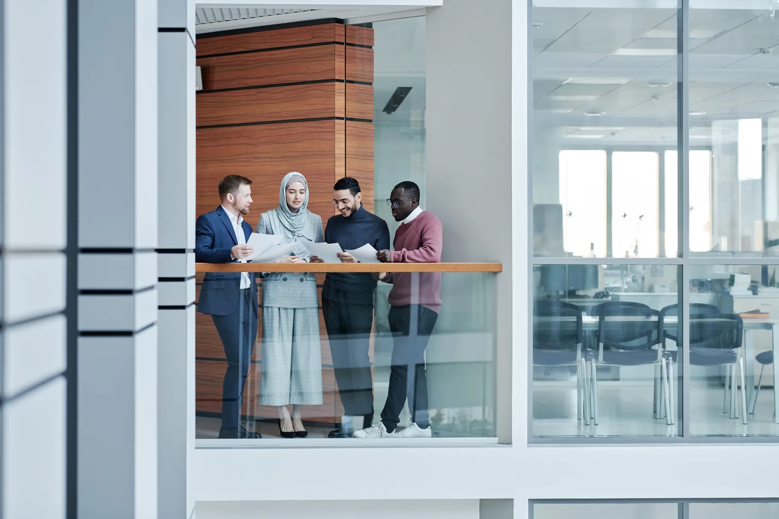 Group of diverse colleagues collaborating in a modern office with glass walls, emphasizing teamwork and inclusivity.