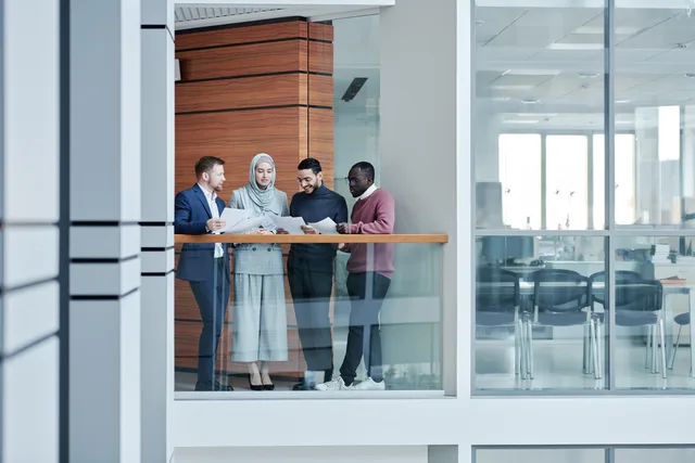 Group of diverse colleagues collaborating in a modern office with glass walls, emphasizing teamwork and inclusivity. Arbetsgivarvarumärket: så bygger ni attraktionskraft på fakta och efterfrågan